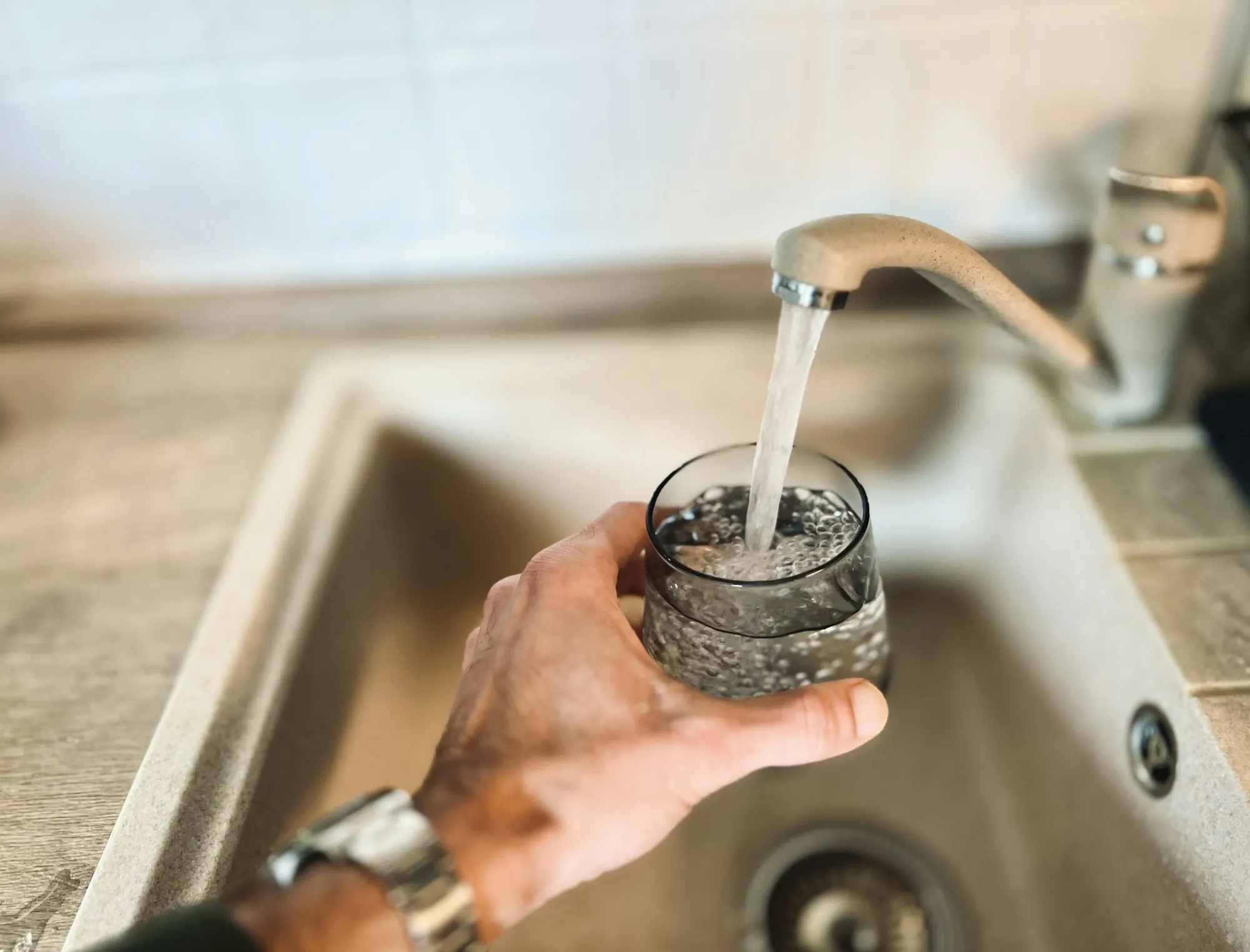 Hand filling a glass with water from a kitchen faucet